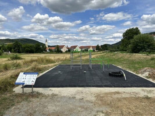 Outdoor-Fitnessbereich mit Klettergerüst, grünen Stangen, Reifen, Seil und malerischer Landschaft im Hintergrund.