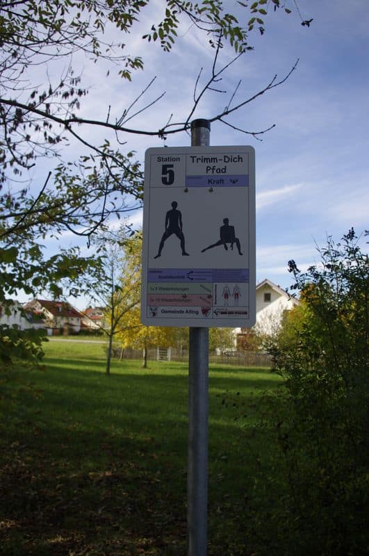 Trim-Dich-Pfad Station 5: Fitness-Übungen in naturschöner Parklandschaft unter blauem Himmel.