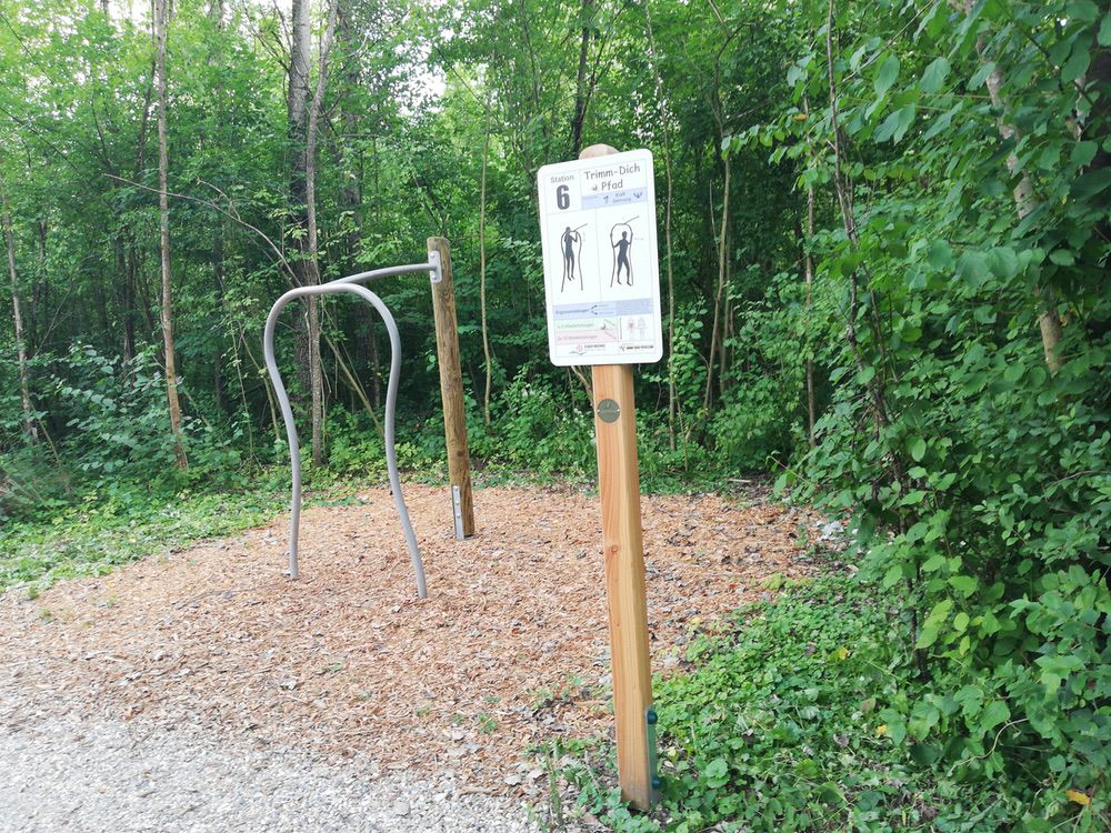 Outdoor Fitnessstation im Wald mit Schildern und Bar für Körpergewichtsübungen, umgeben von Natur.