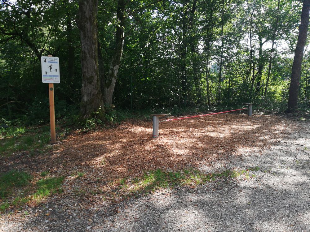 Trimm-dich-Pfad im Wald: Kiesweg, Mulchfläche, Barrieren, Schild mit Informationen und Regeln.