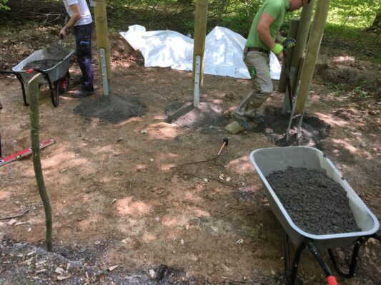 Zwei Arbeiter setzen Betonpfosten im Wald für Bauarbeiten.