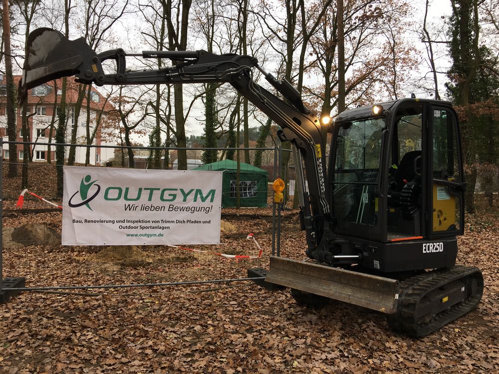 Ausleger baggert im Herbst an einem OUTGYM-Bereich in Wald, nahe Wohngebieten in Deutschland.