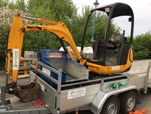 Gelber Bagger auf Tandem-Anhänger, Baustelle im Grünen, robust und sicher transportiert.