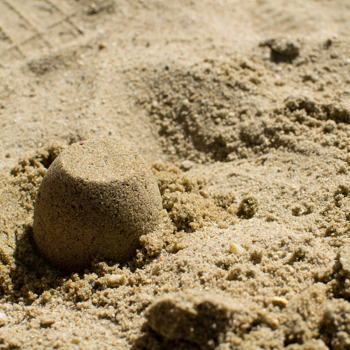 Sandburg am Strand unter sonnigem Himmel, Kindheit, Spiel, Kreativität, Sommertag.