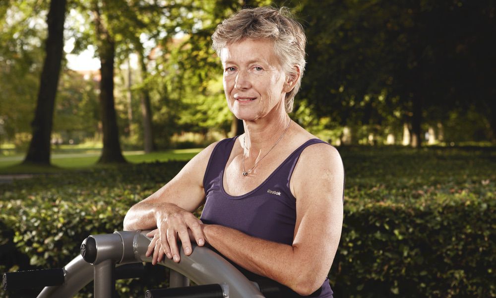 Ältere Frau trainiert im Park auf Fitnessgerät, gesund und aktiv, unter sonnigem Himmel.