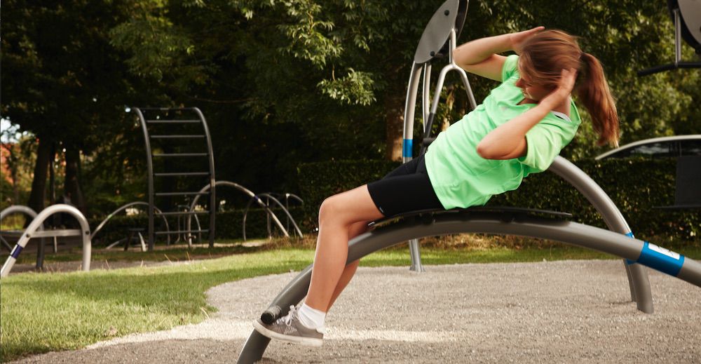 Person macht Sit-ups im Outdoor-Fitnesspark, umgeben von Natur und modernen Sportgeräten.