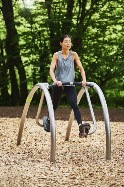 Frau trainiert im Freien mit Fitnessgerät in grüner Naturumgebung.