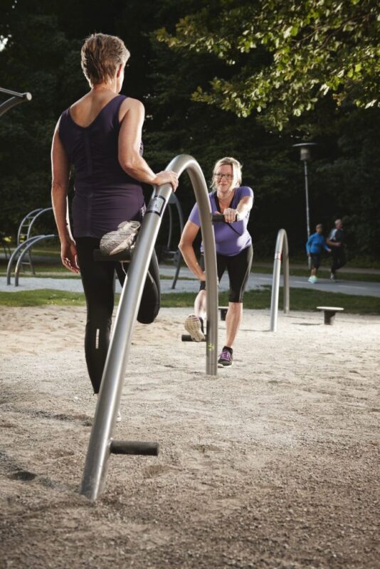 Zwei Frauen beim Outdoor-Training im Park mit Stretchübungen und Gemeinschaftsgefühl.