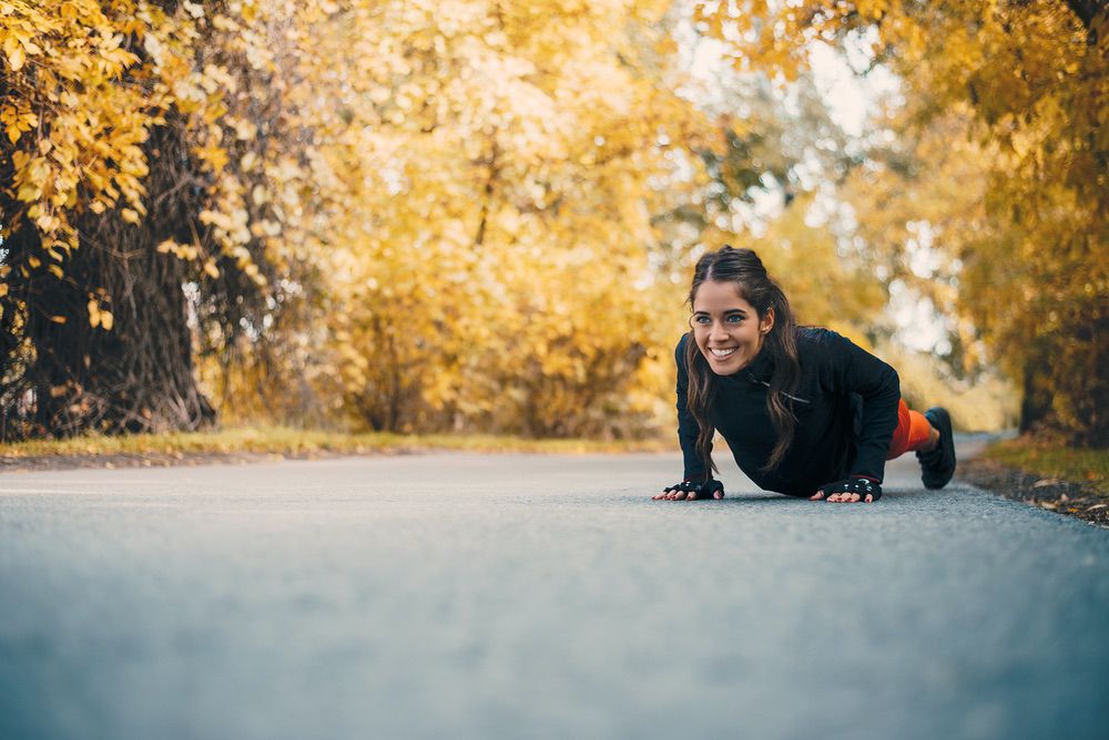 Frau macht Liegestütze im Freien auf einem herbstlichen Weg mit buntem Laub.