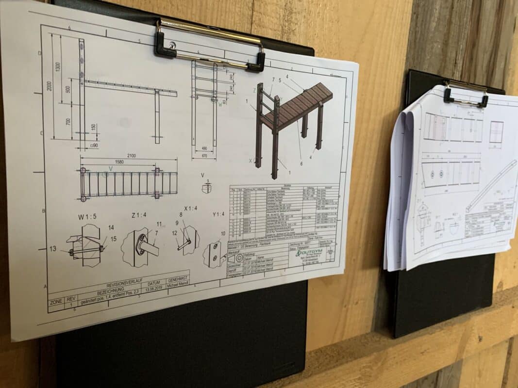 Technische Zeichnungen von Holzbank auf Klemmbrett in Werkstattumgebung.