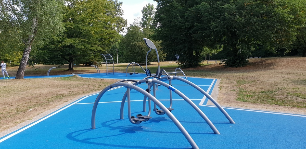 Moderner Outdoor-Fitnessbereich mit blauer Oberfläche und Metallgeräten in einem Park.